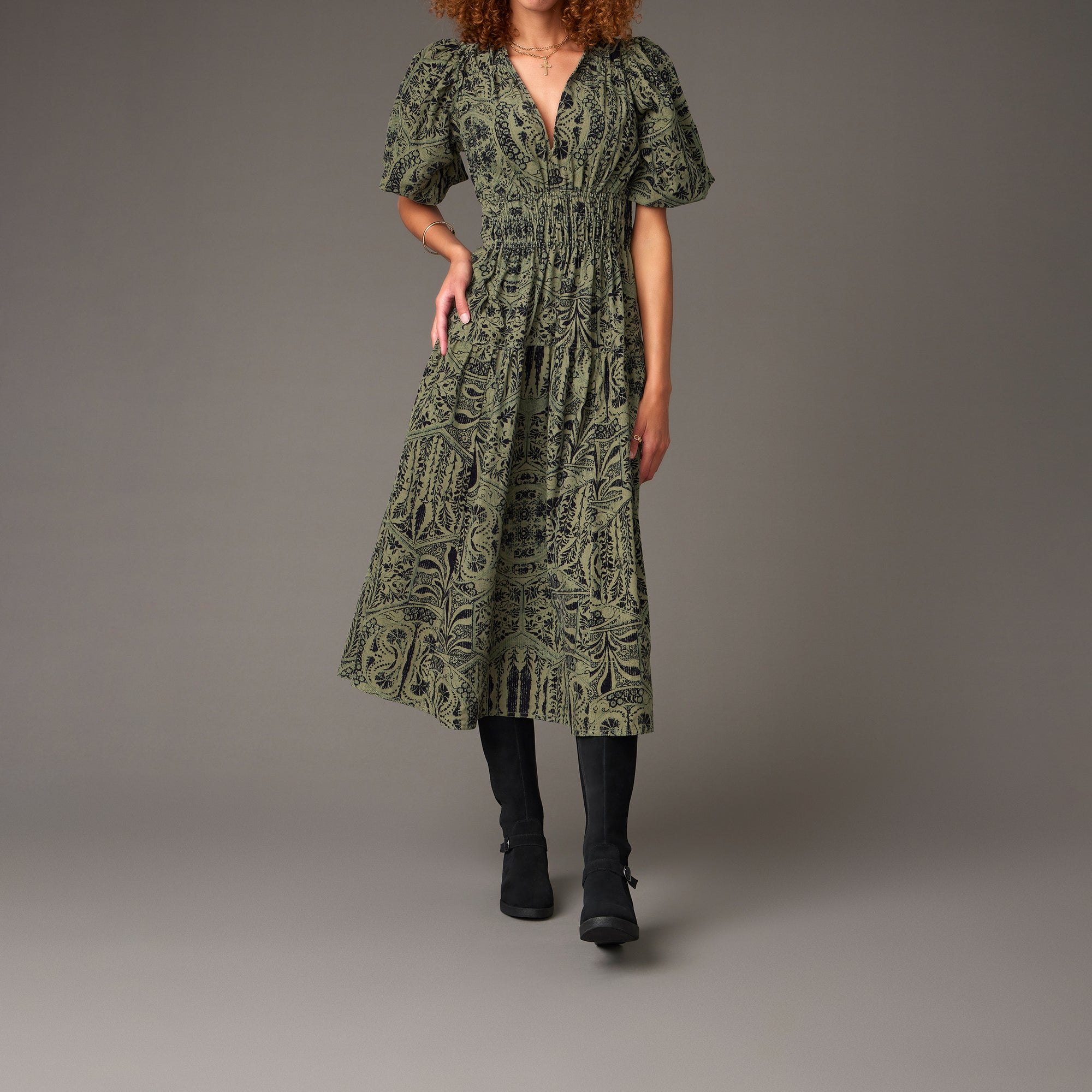 A woman wearing tall-shaft wedge booties with a printed green dress.