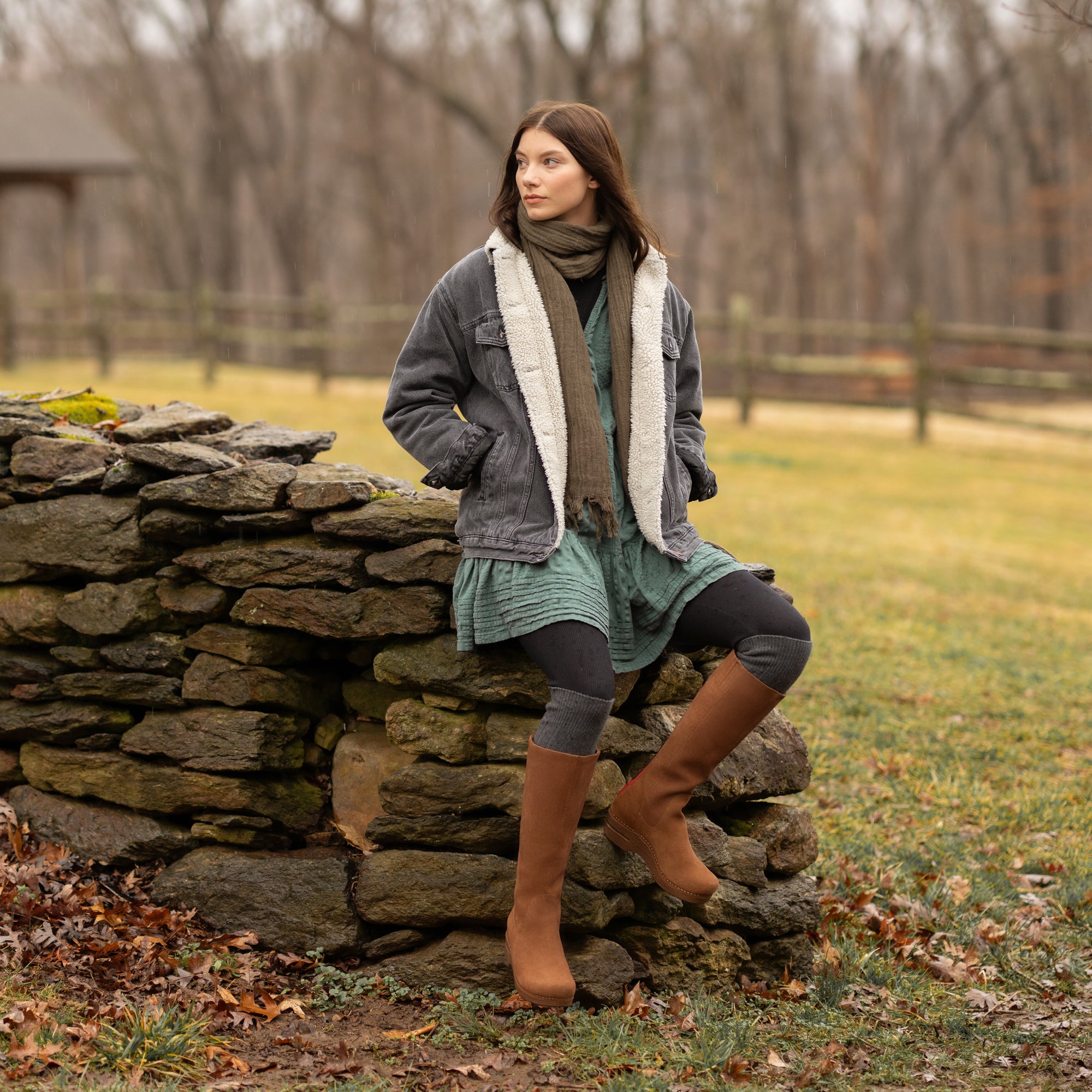 A woman in seasonal attire staying warm with a cozy jacket and brown tall-shaft boots.