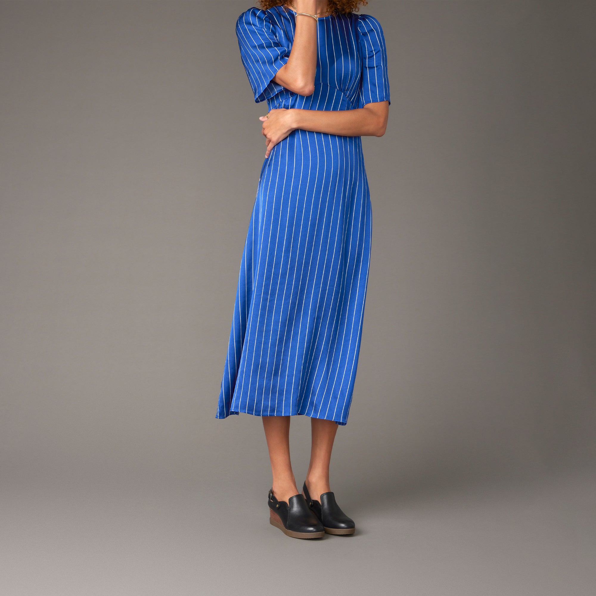 A woman in a blue dress wearing black slingback mules with a leather-stacked wedge heel.