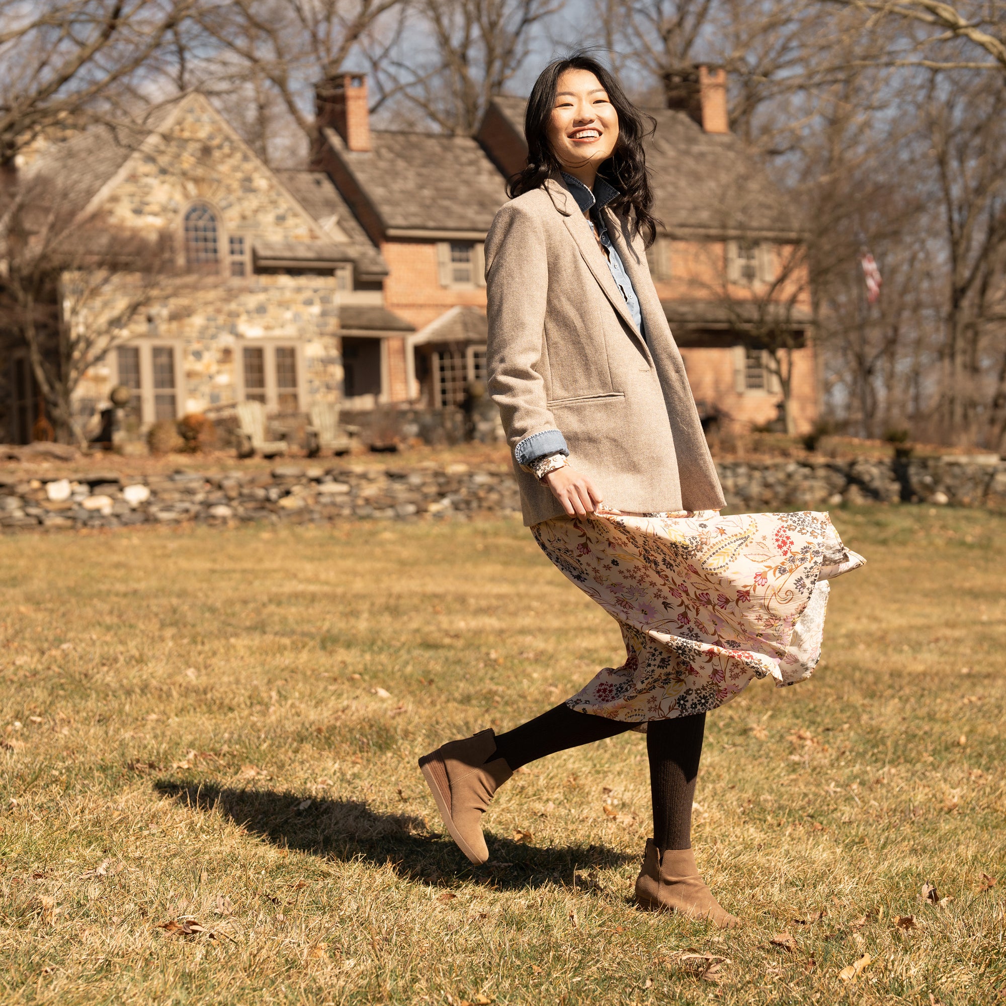 A woman in a field wearing brown wedge booties and a flowery dress.