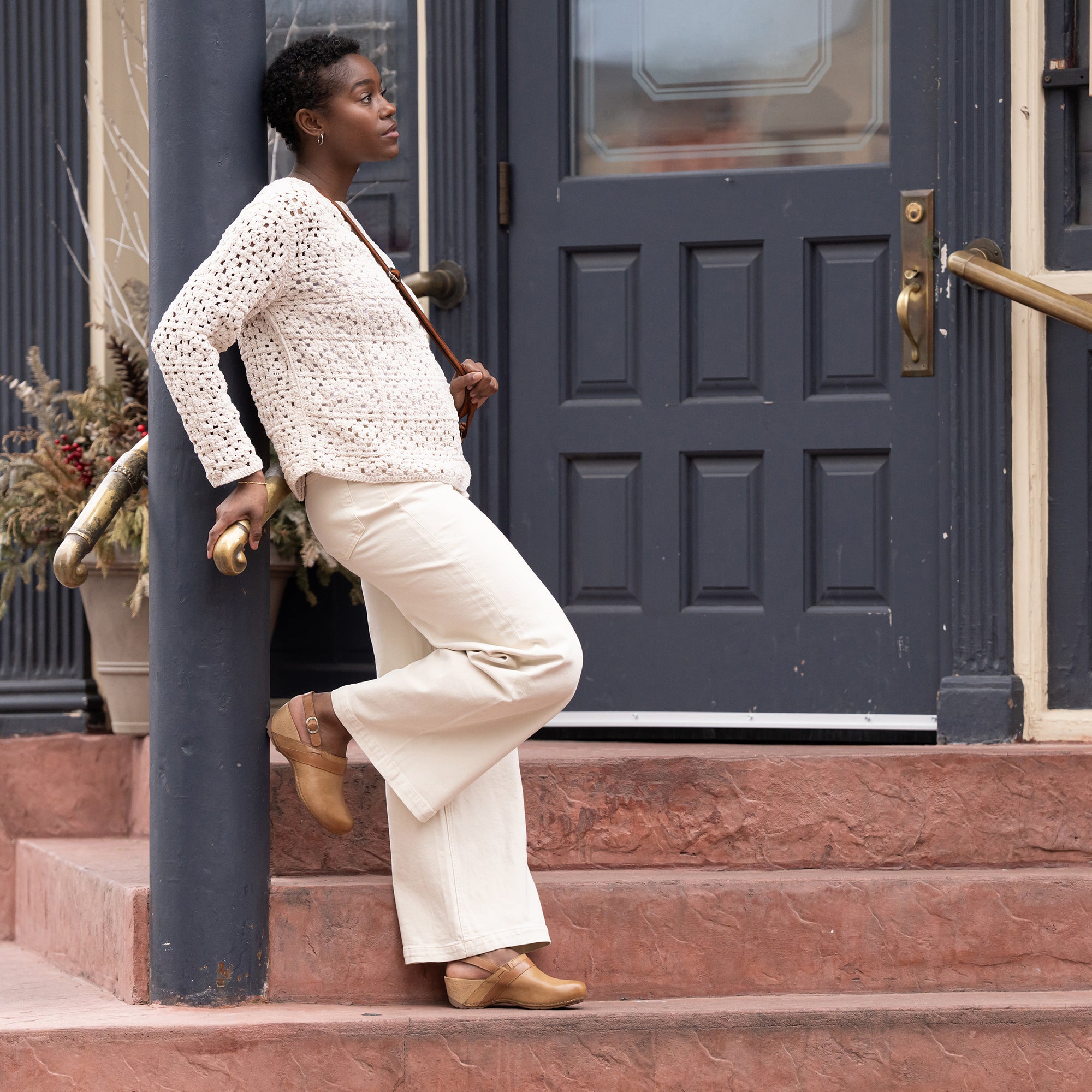 A woman standing in town in a stylish white outfit and tan clogs with a heel strap.