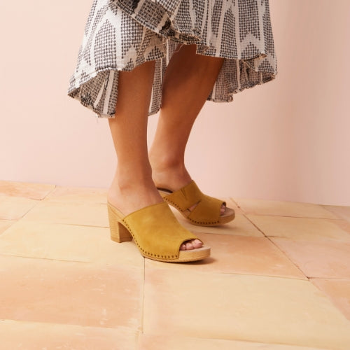 A close up of a peep toe sandal in yellow with a nail head design and high heel.