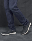 Man in jeans wearing black leather slip-on sneakers.