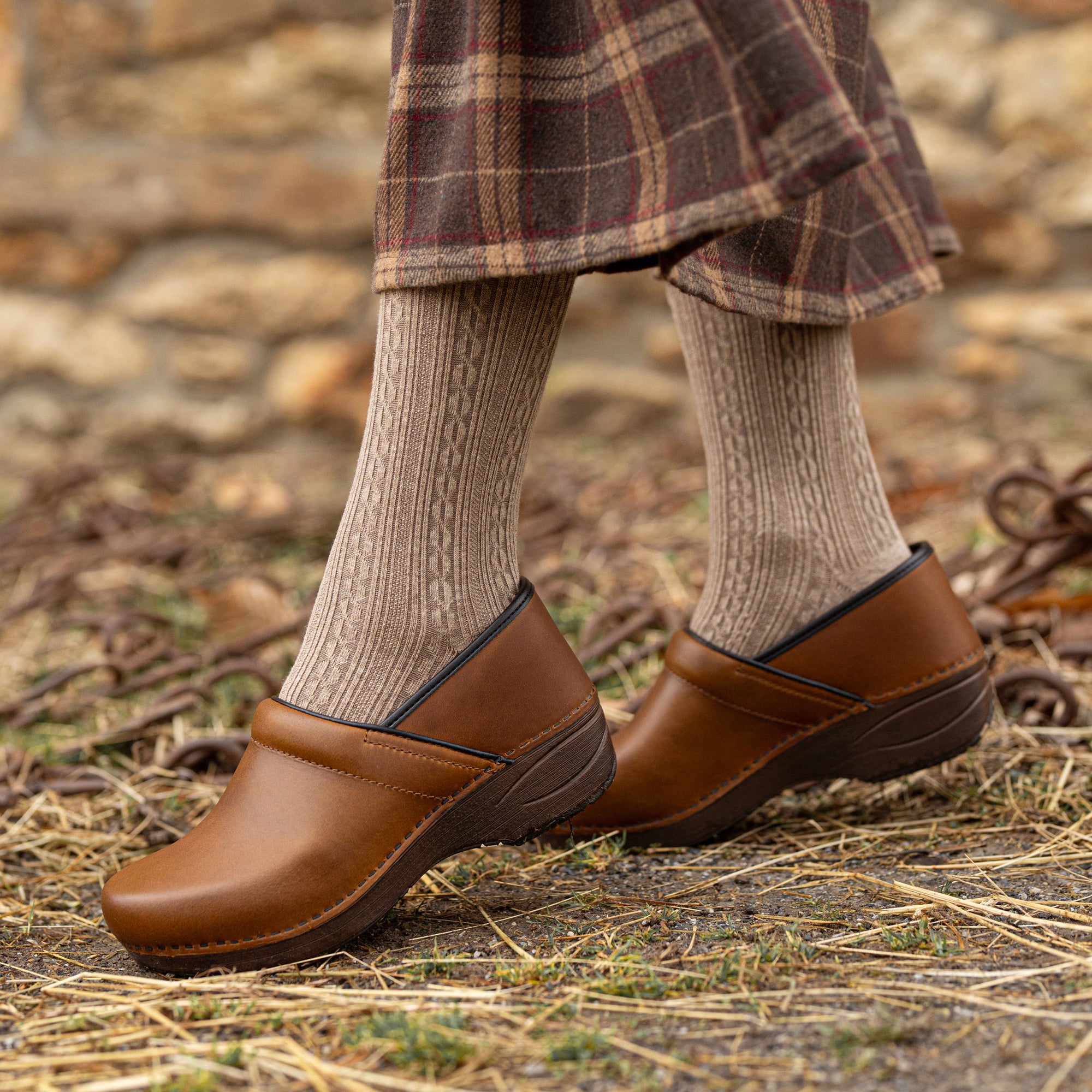 A close up of rich caramel clogs shown on foot.