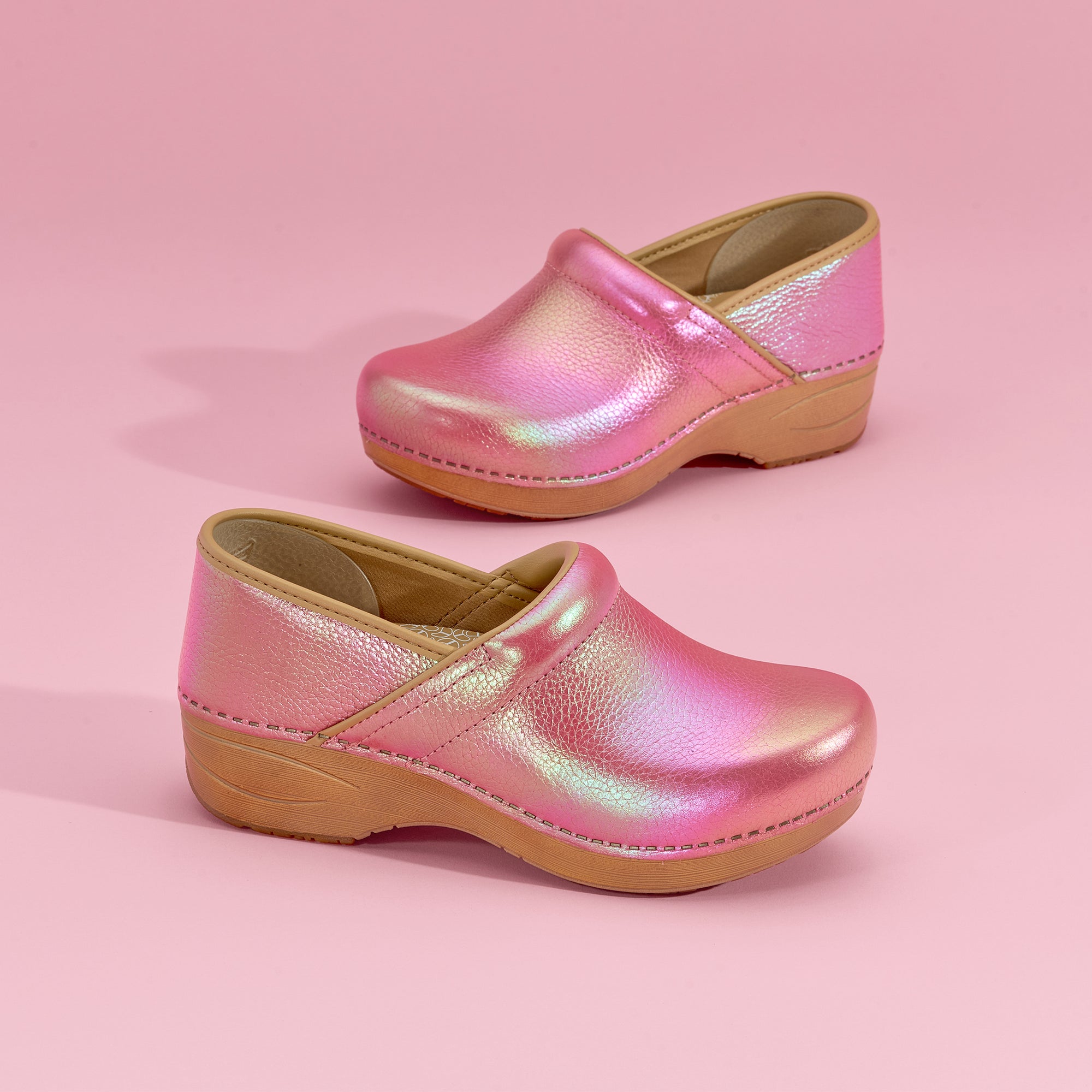 Close up of pink iridescent clogs on pink backdrop.