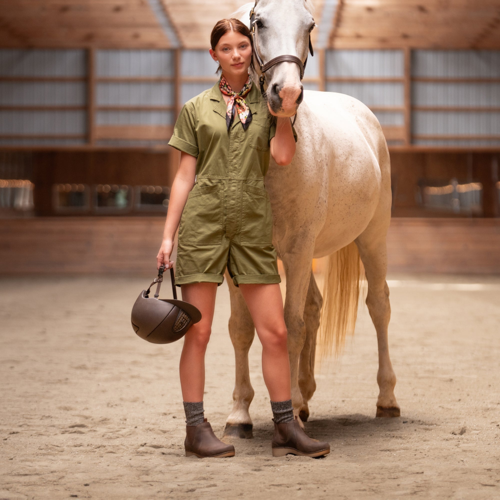 A woman standing with a horse wearing durable brown leather boots.