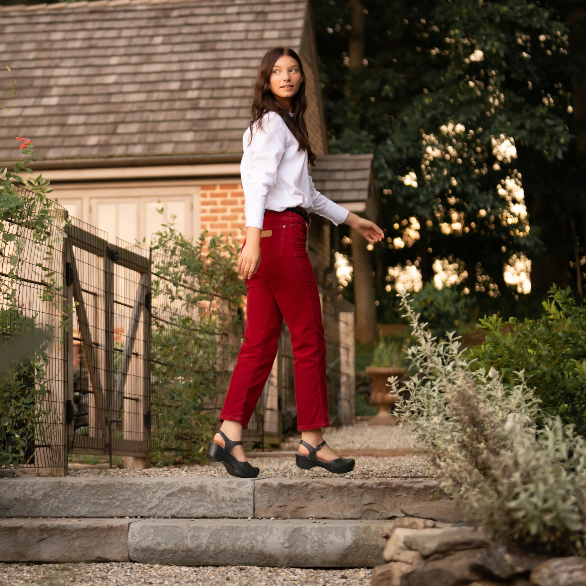 A woman in stylish red jeans wearing black flatform sandals.