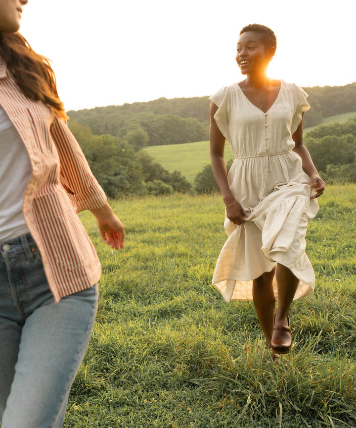 Girl in brown clogs and a white dress walking through a meadow at sunset.