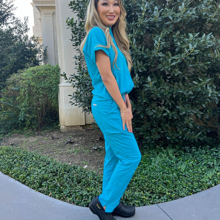 A nurse wearing blue scrubs and black clogs with personalized initials.
