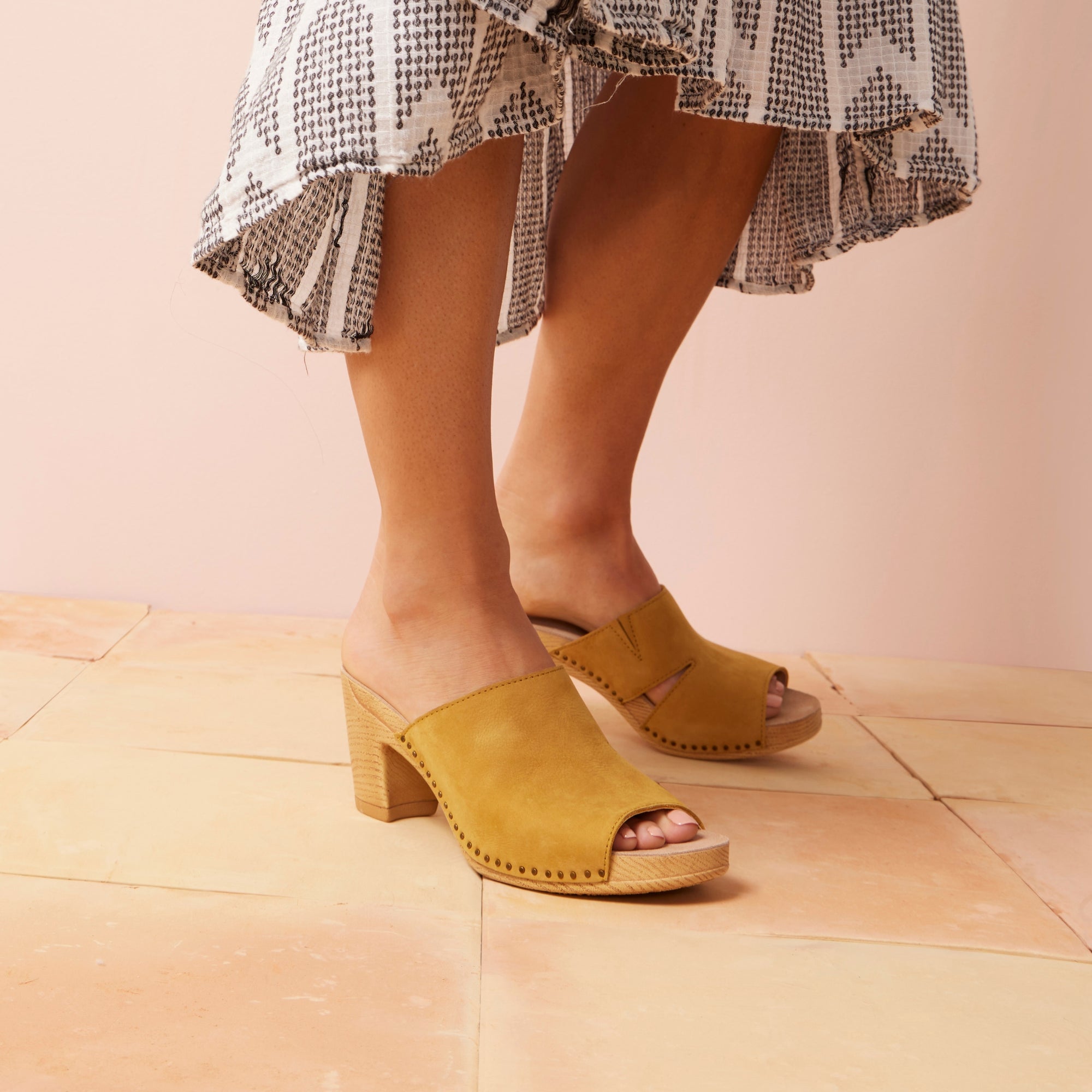 A close up of stylish slide sandals with a high heel and nail head construction.